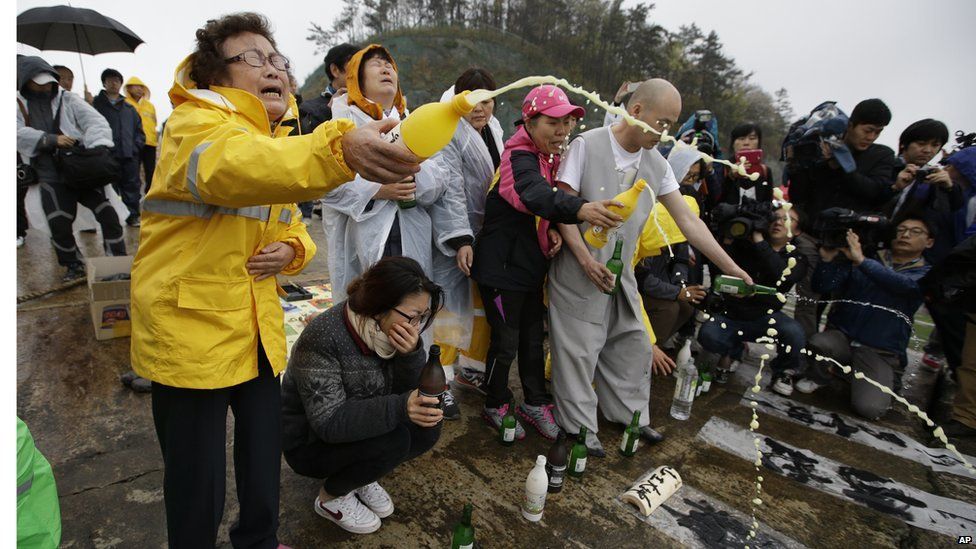 A Buddhist monk and relatives of passengers aboard a sunken ferry spray alcohol during a Buddhist ceremony.