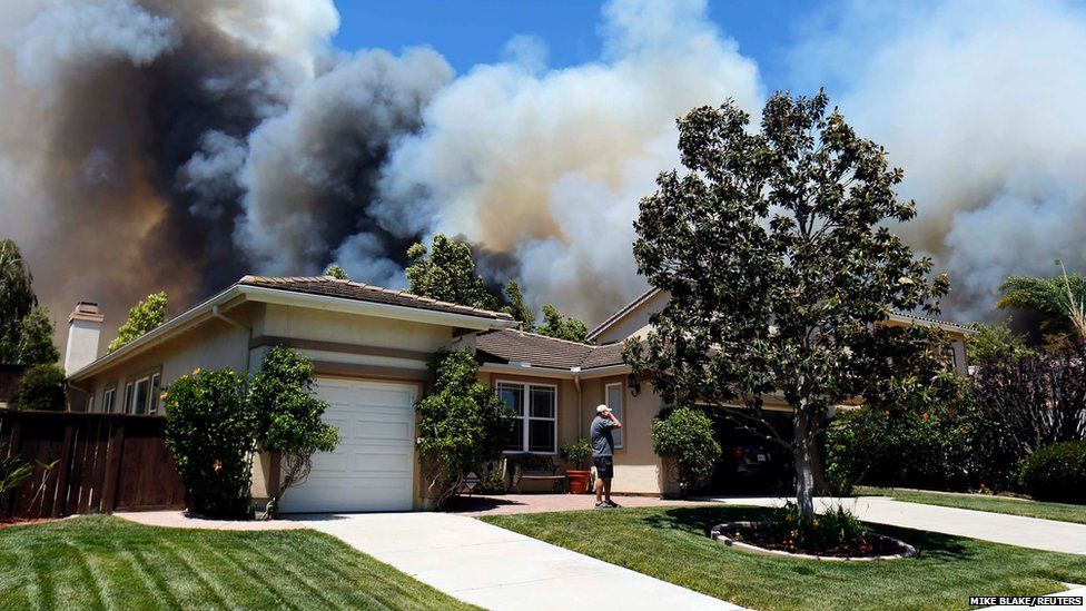 A man talks on a phone as a wildfire is seen approaching the neighbourhood in Carlsbad, California