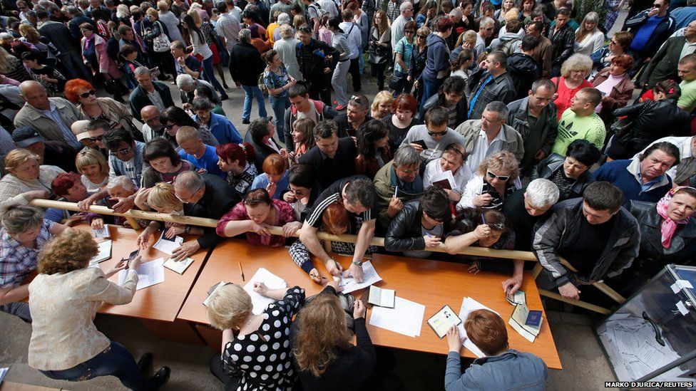 People stand in a line to receive ballots from members (front) of a local election commission during the referendum on the status of Donetsk