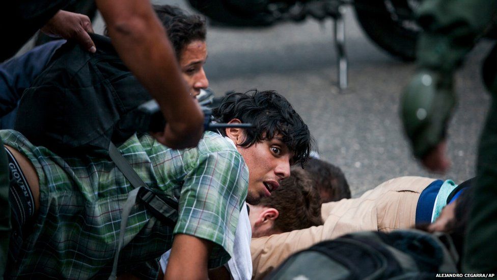 An anti-government demonstrator is held on the ground along with others, as he is detained by the Bolivarian National Guard