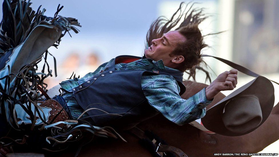 Kyle Brennecke loses his hat as he flies backwards during the bareback bronc riding event at the Reno Rodeo in Nevada