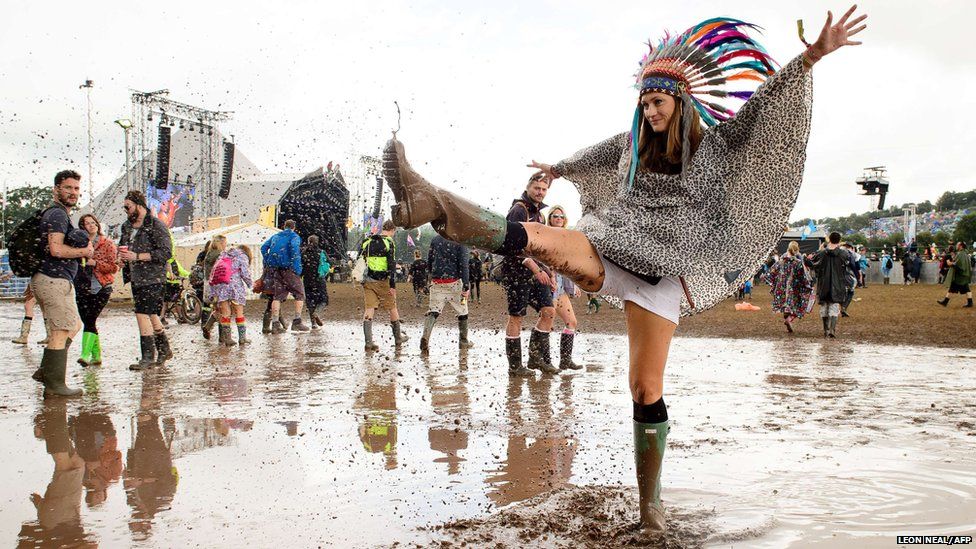 A woman kicks water in a puddle as she poses for photographers, on the first official day of the Glastonbury Festival