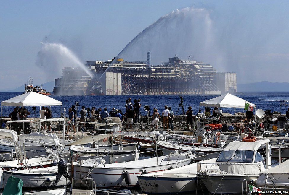 Tugboats send up water sprays as the wrecked Italian cruise liner the Costa Concordia begins its final journey to the port of Genoa