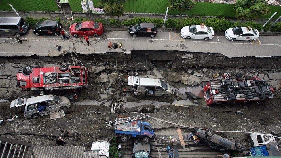 Two fire engines and other vehicles lie on their side on a caved-in road caused by underground explosions in Kaohsiung City, southern Taiwan, on 1 August 2014