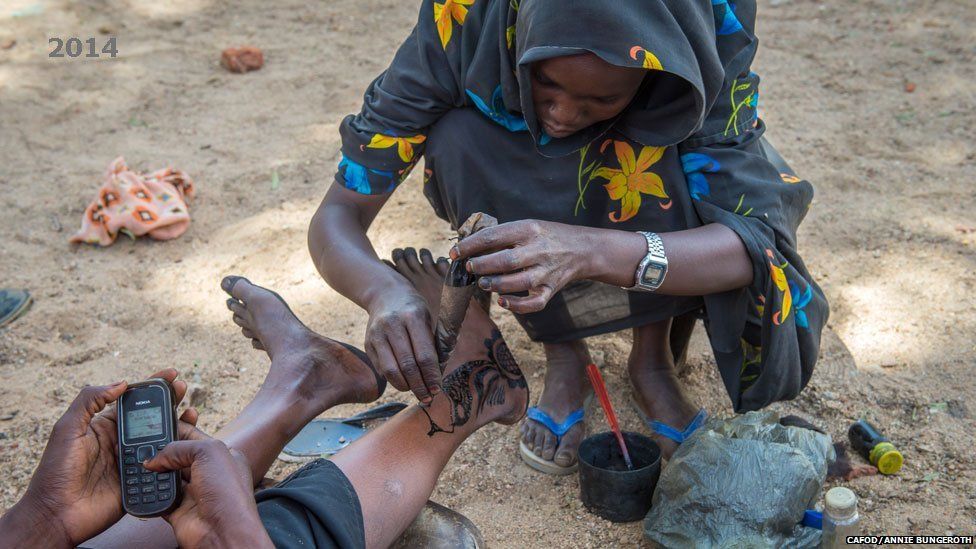 A woman applies a henna dye pattern to another's legs in Hassa Hissa camp in Darfur, Sudan - 2014
