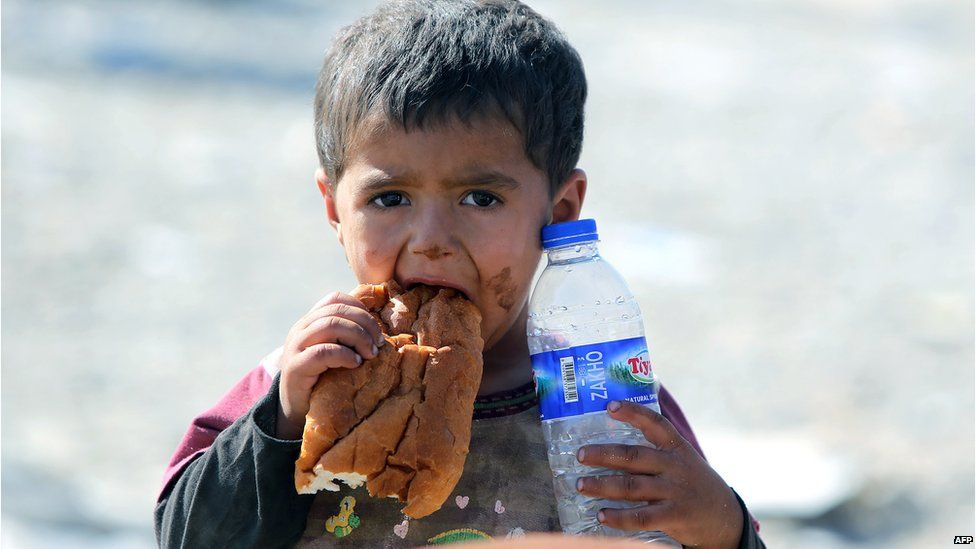A displaced Iraqi boy from the Yazidi community eats a piece of bread and holds a bottle of water as they cross the Iraqi-Syrian border at the Fishkhabur crossing, in northern Iraq, on 11 August 2014.