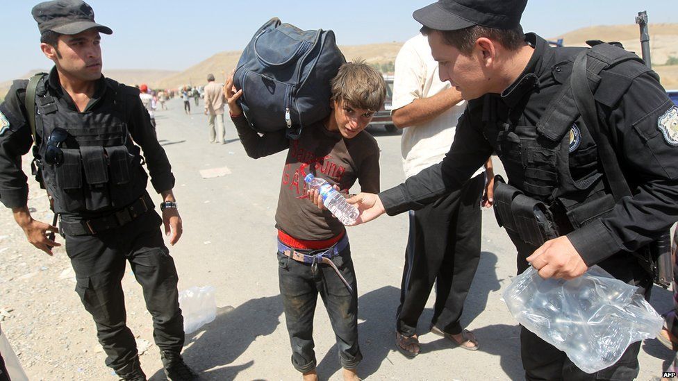 Peshmerga forces hand out water bottles to displaced Iraqi families from the Yazidi community as they cross the Iraqi-Syrian border at the Fishkhabur crossing, in northern Iraq, on 11 August 2014.