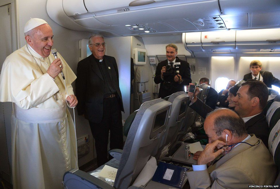 Pope Francis smiles as he welcomes journalists aboard the flight to Seoul