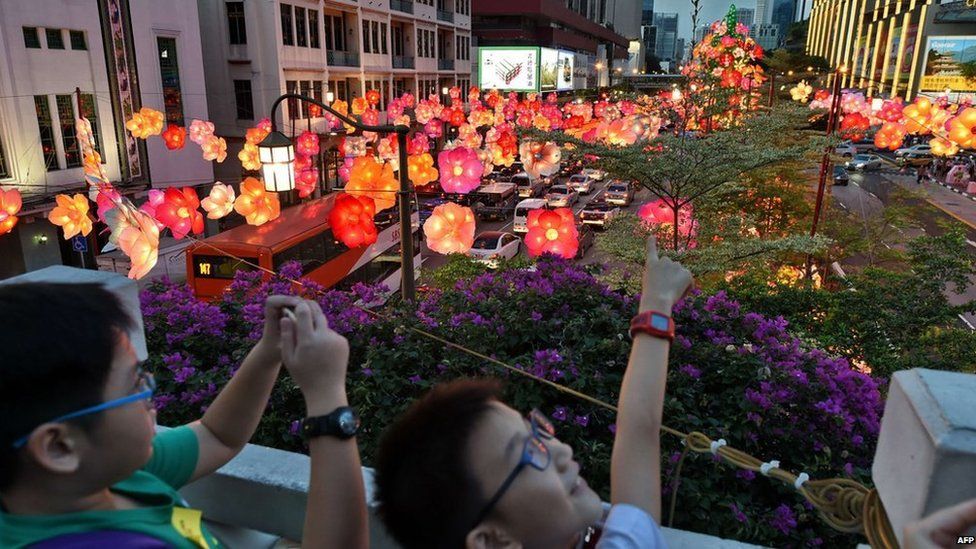 Children look at floral lanterns hang above a street during a media preview of the upcoming mid-autumn festival in Singapore on 31 August, 2014