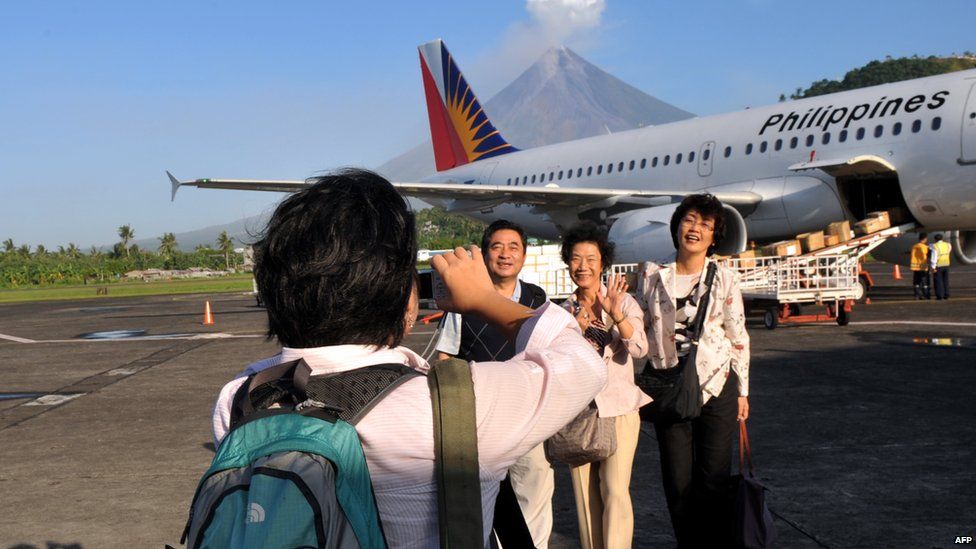 Foreign tourists have their photos taken at the airport with the back drop of Mayon volcano spewing ash into the air in Legazpi City, Albay province, southeast of Manila on 24 December 2009