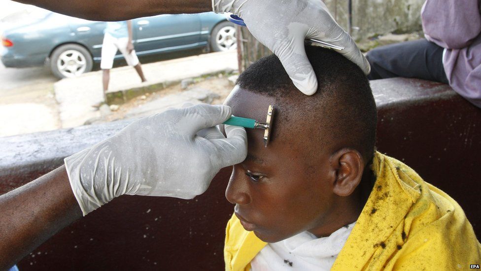 A barber wearing latex gloves shaving a client's head, Monrovia, Liberia - Friday 12 September 2014