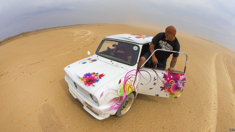 A photograph taken with a fish eye lens of a South African man climbing into a modified Mini Cooper during the 2014 Kalahari Desert Speedweek at Hakskeenpan, Northern Cape of South Africa, 23 September 2014
