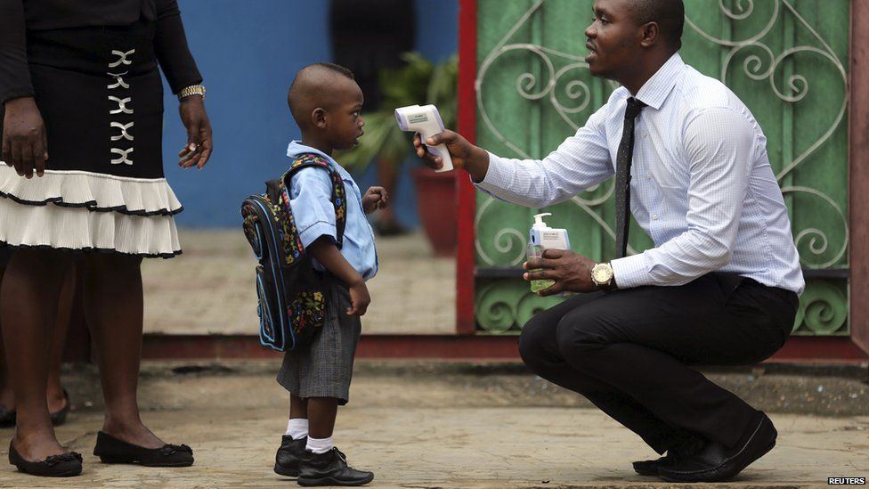 A school official takes a pupil's temperature using an infrared digital laser thermometer in front of the school premises, at the resumption of private schools, in Lagos on 22 September 2014