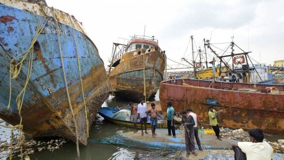 People stand on boats damaged by strong winds caused by Cyclone Hudhud in the southern Indian city of Visakhapatnam October 13, 2014.
