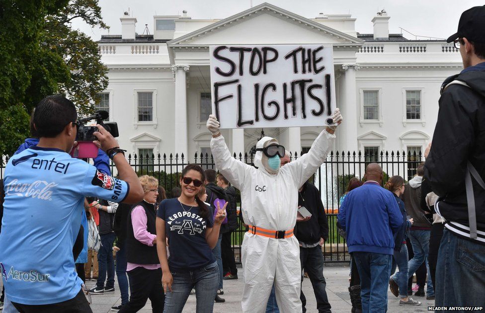 A tourist poses for a photo next to Jeff Hulbert from Annapolis, Maryland, who is dressed in a protective suit and mask demanding for a halt of all flights from West Africa, outside the White House in Washington DC