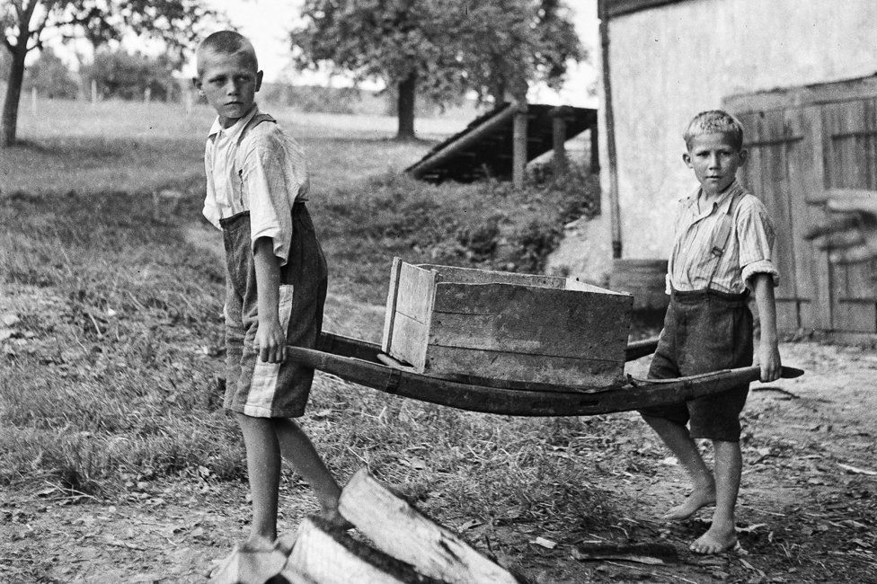 Two boys with no shoes carrying a crate