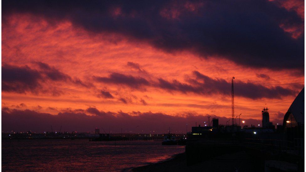 Fiery red skies over a darkened sea and shore. The bright red sky reflects off the water.