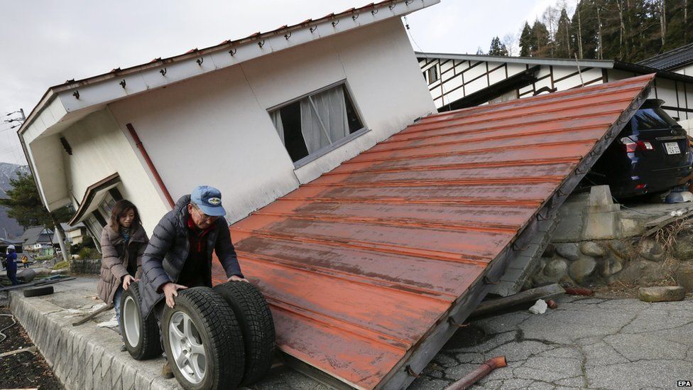 Residents roll winter tyres past houses damaged after a 6.7-magnitude earthquake in the ski resort village of Hakuba, central Japan (23 November 2014)
