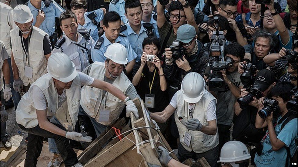 Journalists gather as workers assist bailiffs in removing a barricade under a court injunction in the Mongkok district of Hong Kong on November 25, 2014