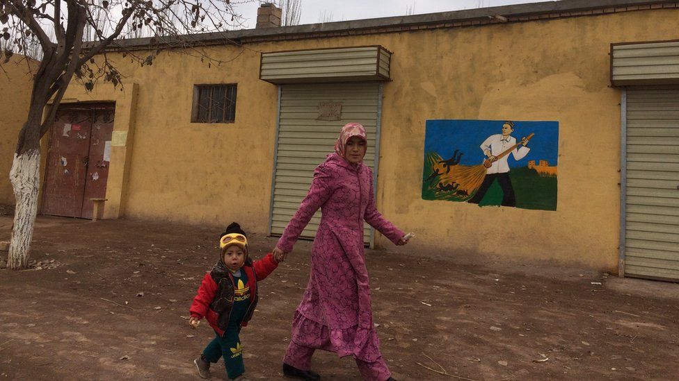 A woman and child walk past a building with a mural painted on its side