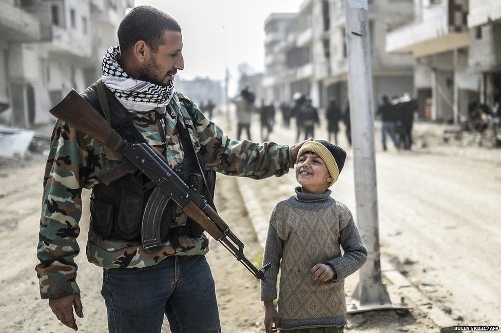 A Kurdish fighter walks with his child in the center of the Syrian border town of Kobane