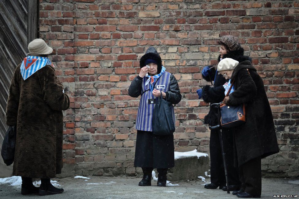 A Holocaust survivor wipes her eye while standing along with others outside a detention block of the Auschwitz Nazi death camp in Oswiecim, Poland