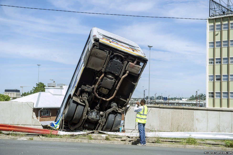 A South African emergency services marshal takes a picture of a public transport bus that drove over the side of Queen Elizabeth bridge in Johannesburg