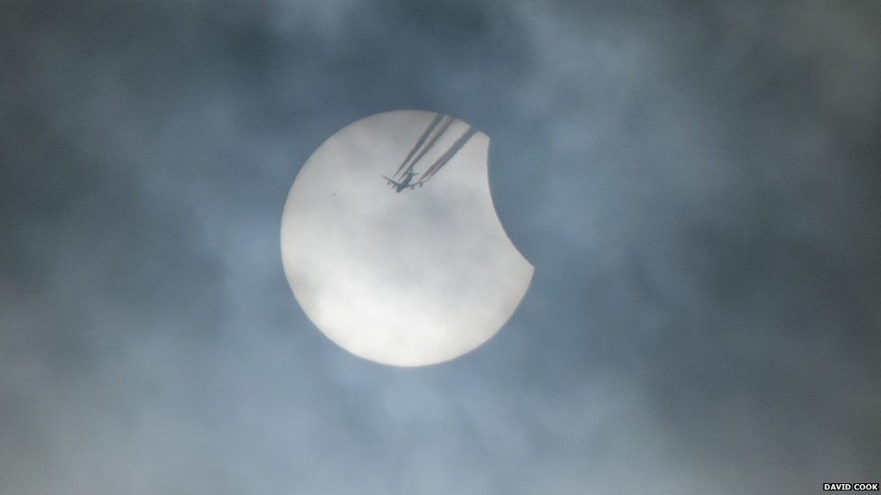 A plane passes by the sun during the initial stages of the solar eclipse over Blackburn, England