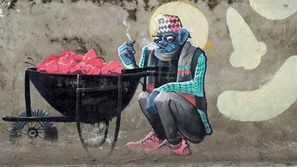 Mural shows a blue man enjoying a cigarette sitting by a wheelbarrow full of hearts