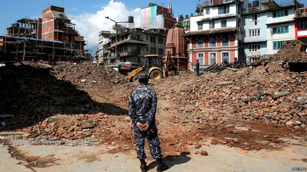 A member of Nepalese police personnel looks on as an excavator is used to dig through rubble to search for bodies, in the aftermath of Saturdays earthquake in Kathmandu (27 April 2015)