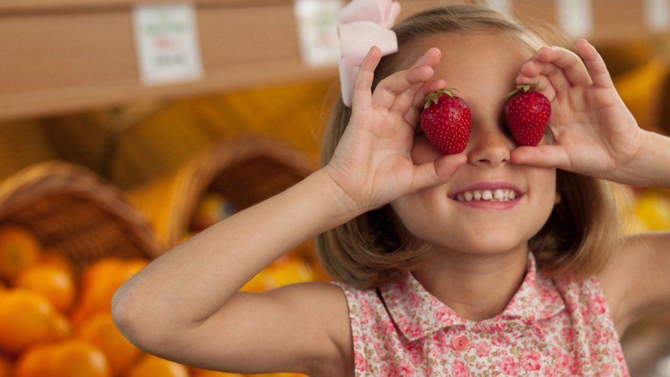 Girl holding strawberries over her eyes