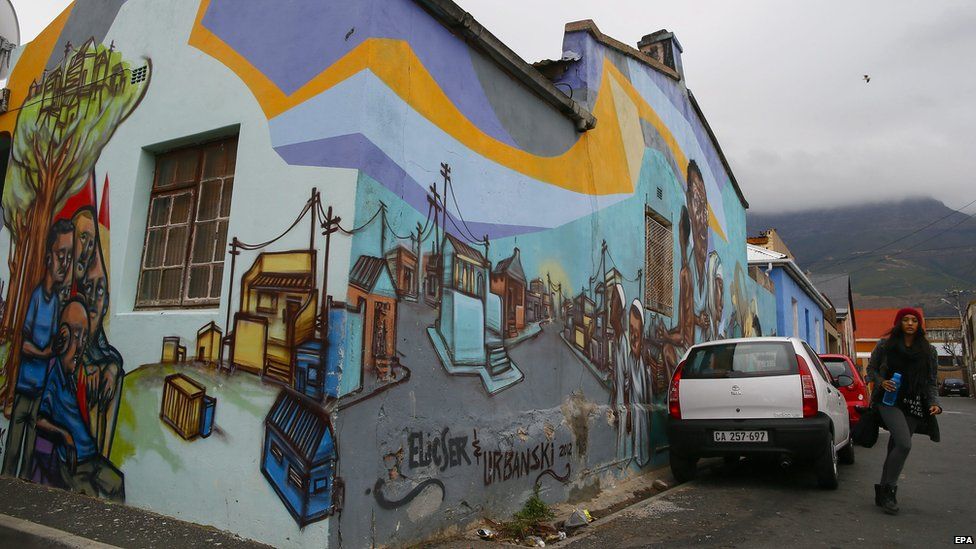 A South African woman walks past street art on a house in Woodstock, Cape Town on Thursday 21 May 2015