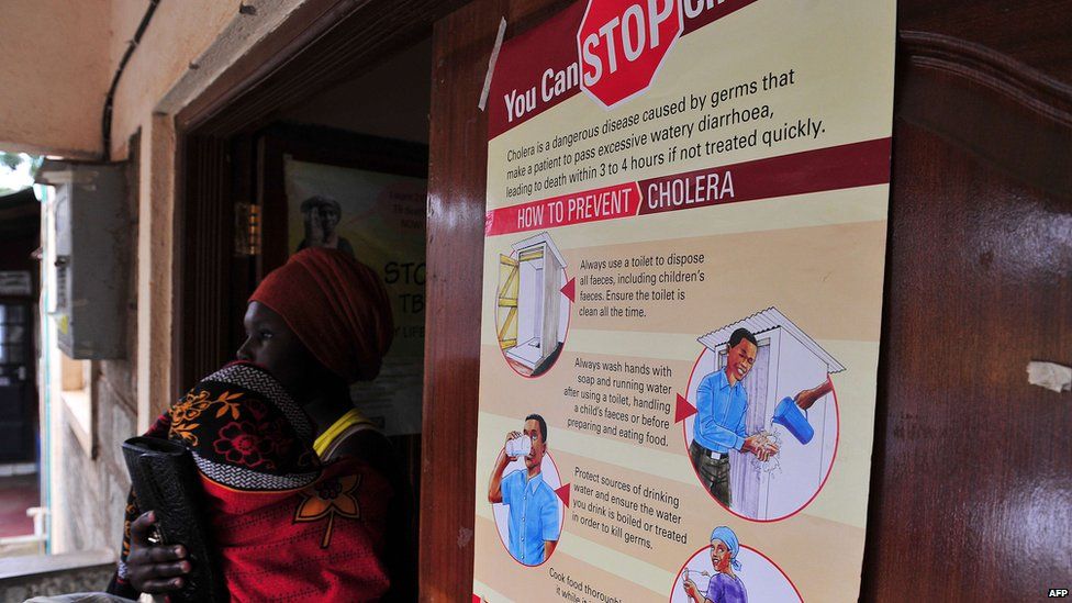 A woman holding a baby walks past a poster with information about cholera at a hospital in the Kibera area of Nairobi, Kenya - 20 May 2015