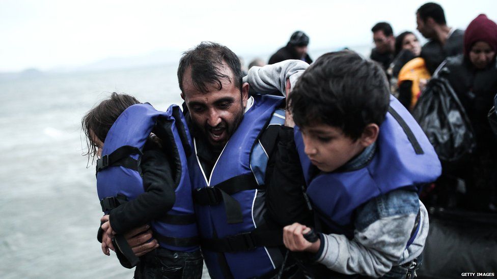 Migrants, including a man carrying two children, arrive on the beach by boat