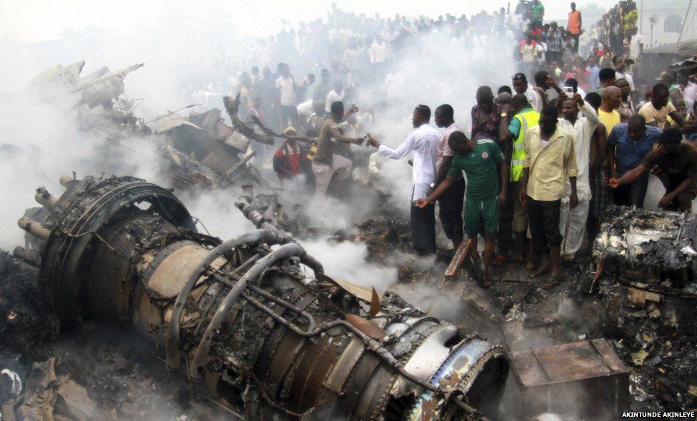 A man in the crowd takes a picture as the smoke bellows out of the plane that fell down in Lagos in 2013. It crashed into a printing works and burst into flames on its way from Abuja. There were later reports of people trying to loot the wreckage 1 June 3, 2012 Agege, Lago
