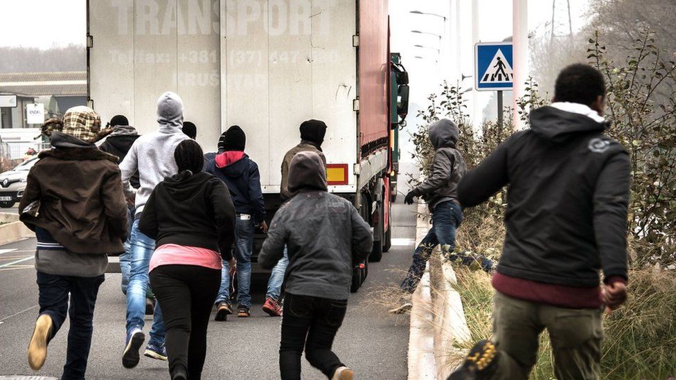 Migrants run behind truck