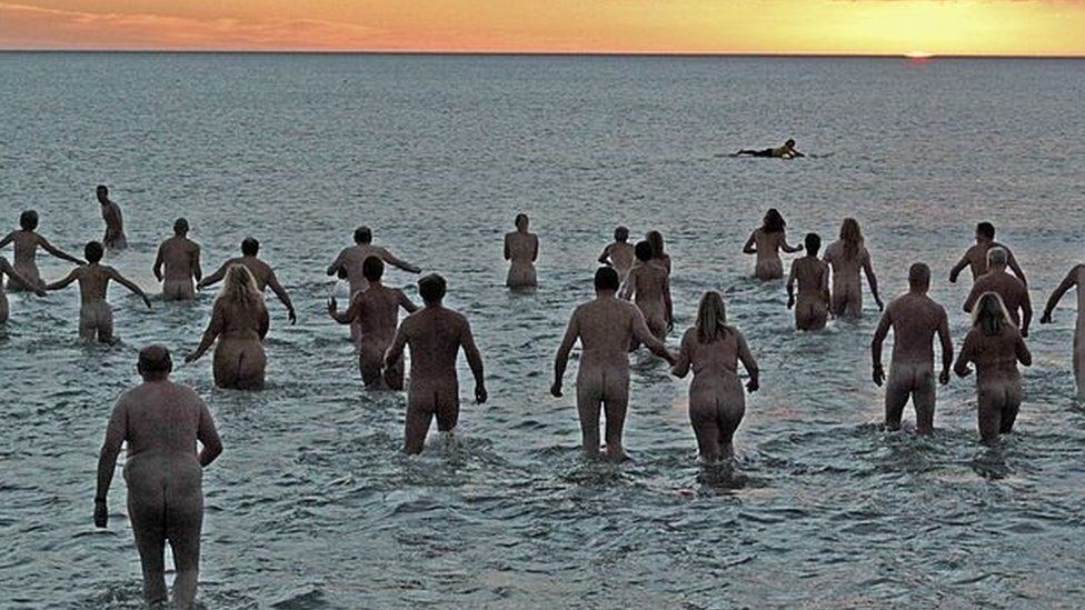 Hundreds of nudist people running into the sea naked