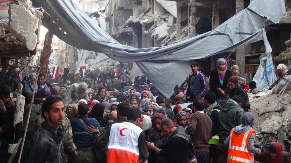 Crowds of Yarmouk camp residents wait to be allowed to join the queue for aid distribution
