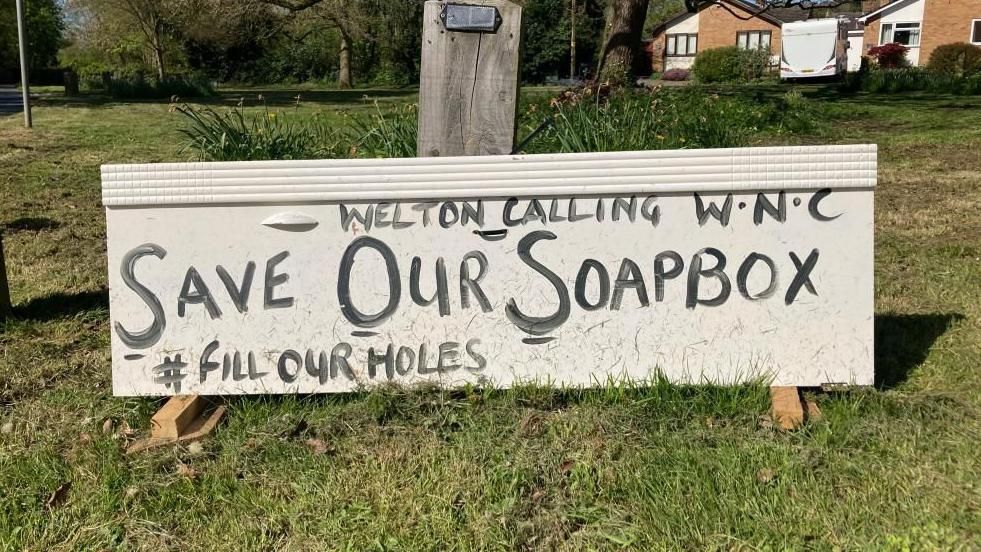 A sign in block capitals calling on West Northamptonshire Council to save Welton's soapbox