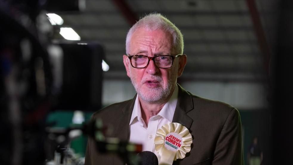 Jeremy Corbyn wearing a white, independent, rosette with his name on