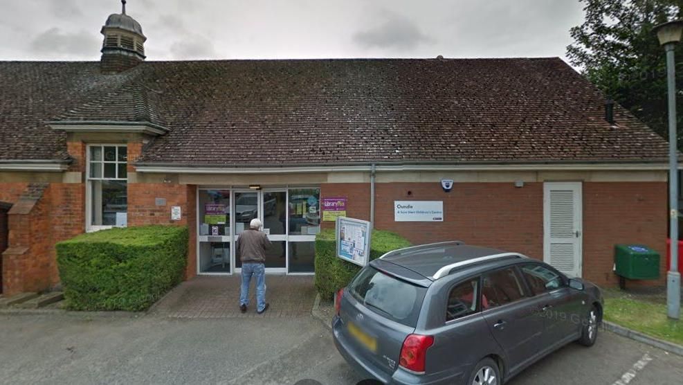 Single-storey section of brick-built library building with small cupola on roof and "library plus" sign by door