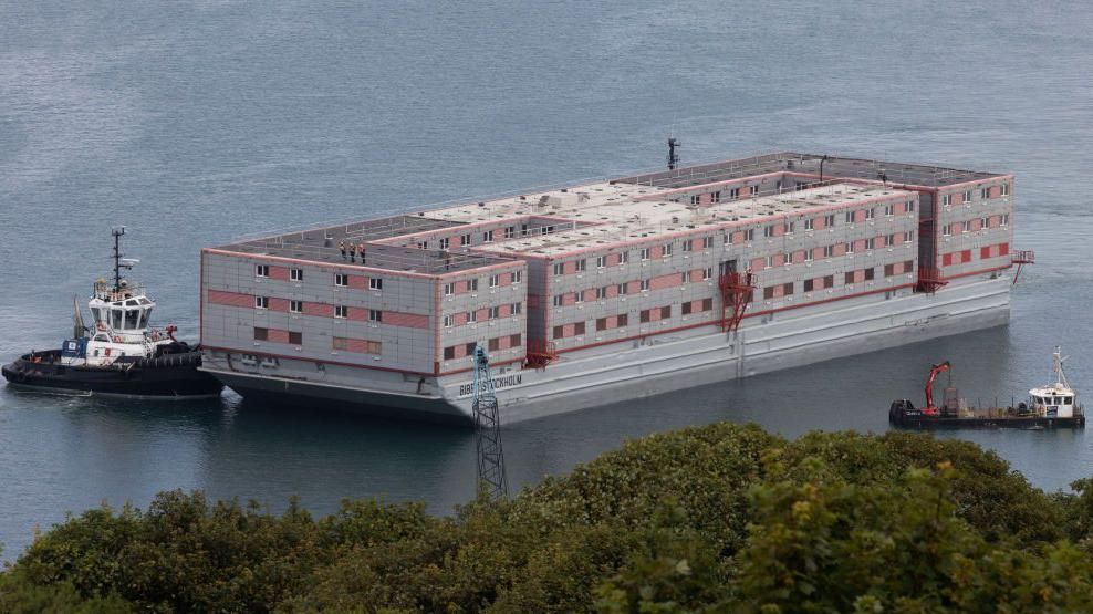 A grey and red barge being tugged through the sea.