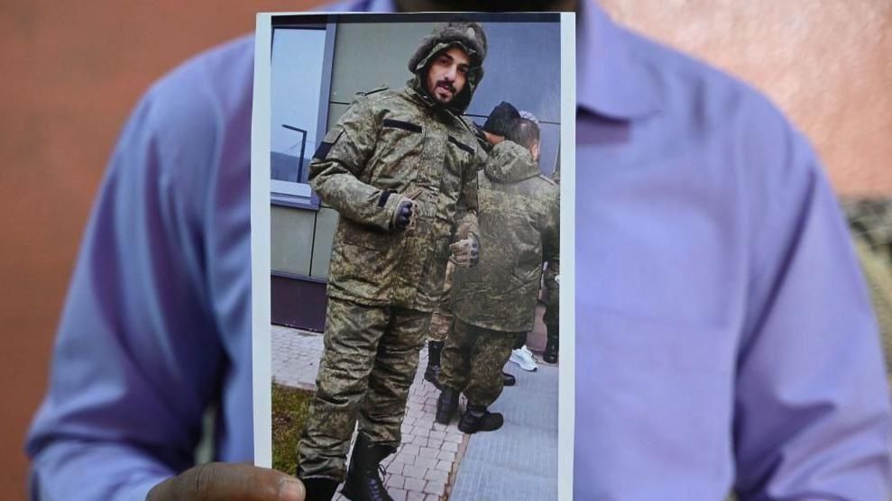This photo taken on February 22, 2024 shows a picture printout of Indian national Mohammed Asfan, seen wearing Russian military fatigues who last called family from the southern Russian city of Rostov-on-Don before being deployed amid the conflict in Ukraine, being held by his brother Mohammed Imran in Hyderabad