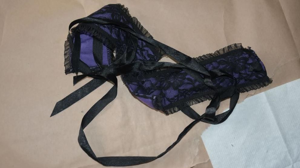 A police evidence photo of purple and black handcuffs made from lace and ribbon material, placed on brown paper