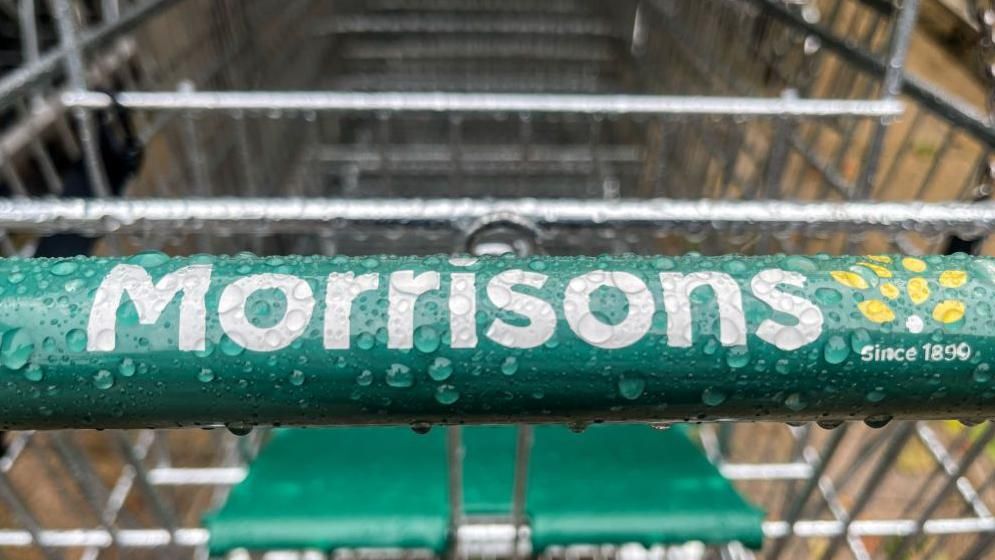 The Morrisons logo on a Morrisons shopping trolley with rain on it 