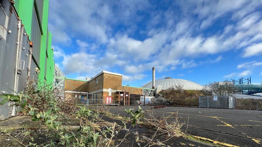 A shot looking up at the Oasis site in Swindon, overgrown, red brick buildings and dome in the background