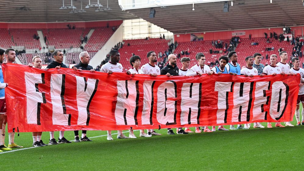 Bristol City players lined up on the football pitch holding a banner which reads: "Fly high Theo"