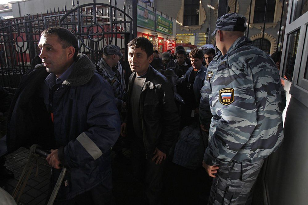 Migrant workers pass policemen as they board a train bound for Tajikistan in Moscow, October 7, 2011