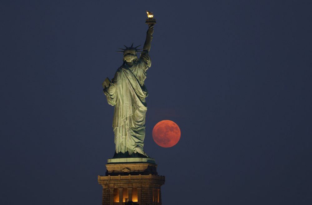 A 99.7 por ciento iluminada Luna Buck se eleva a través de una bruma detrás de la Estatua de la Libertad en la ciudad de Nueva York el 2 de julio de 2023