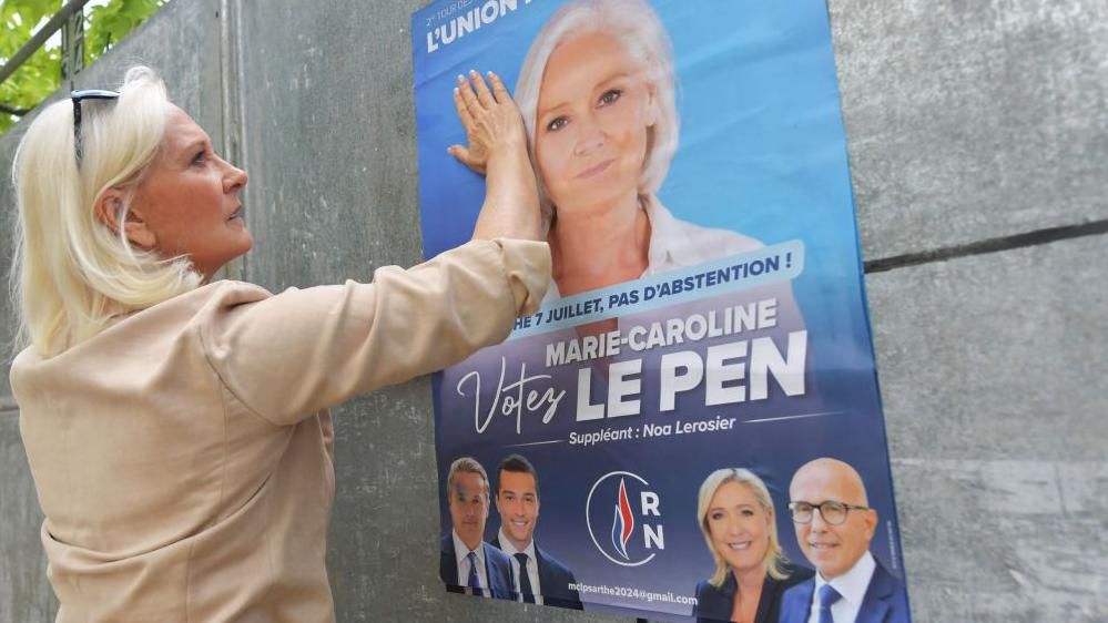 French far-right National Rally (RN) party member and candidate for the second round of legislative elections Marie-Caroline Le Pen, puts her hand on a campaign poster in Brains-Sur-Gée, western France